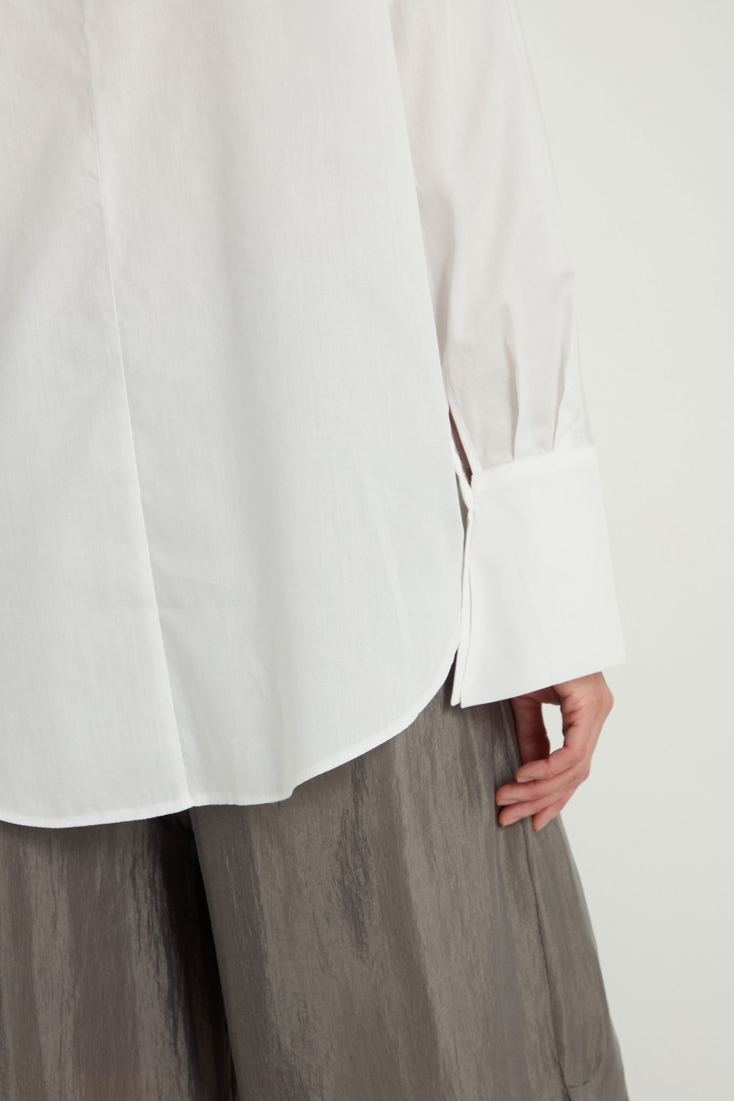 A person modeling the Bamboo Print Shirt, a pure cotton white long-sleeve top with wide cuffs, paired with loose gray pants. Only the torso and one hand are visible.