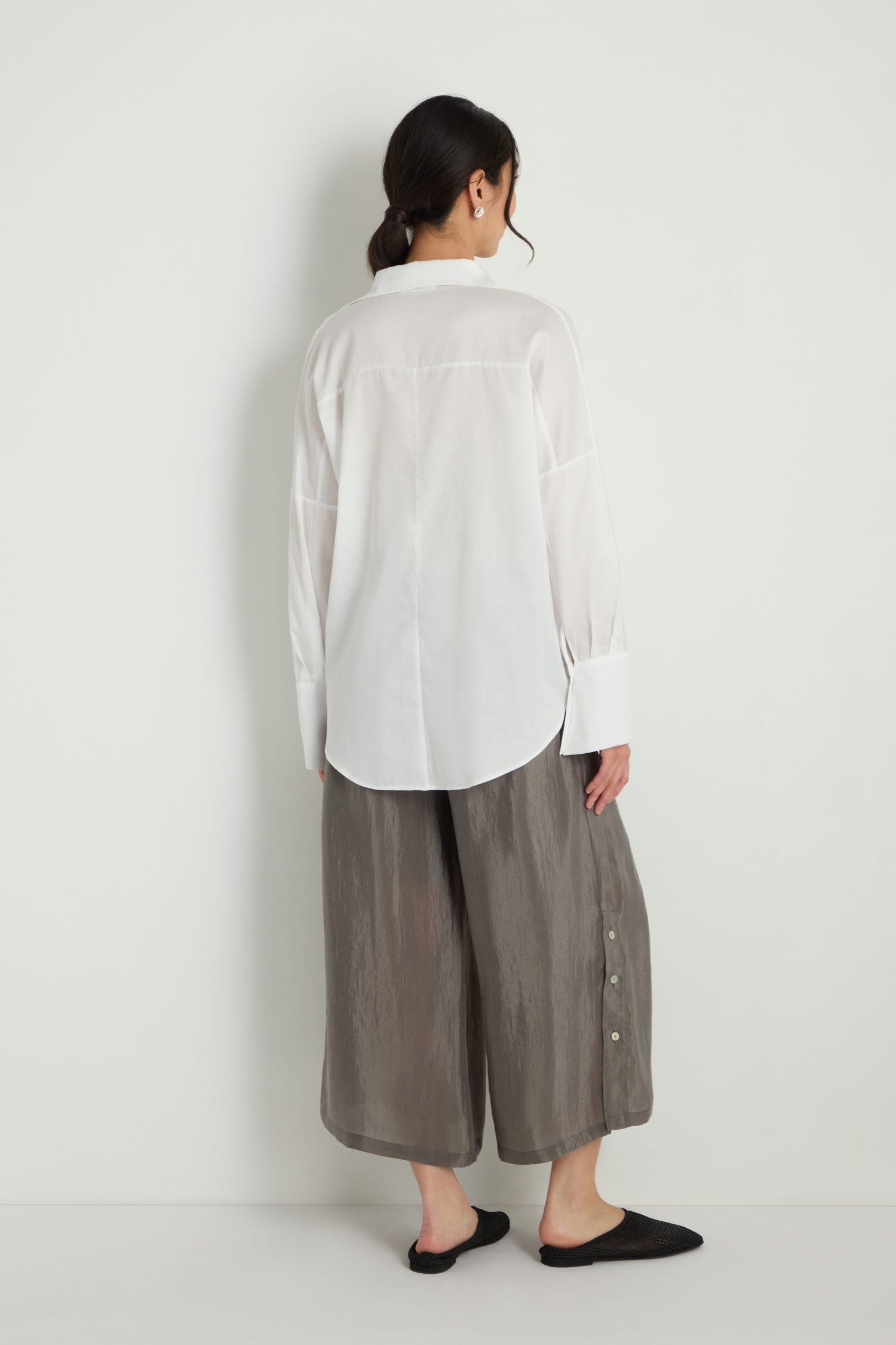 A woman faces away, wearing the Bamboo Print Shirt and loose gray wide-leg pants with side buttons, paired with black flat shoes against a plain white background.