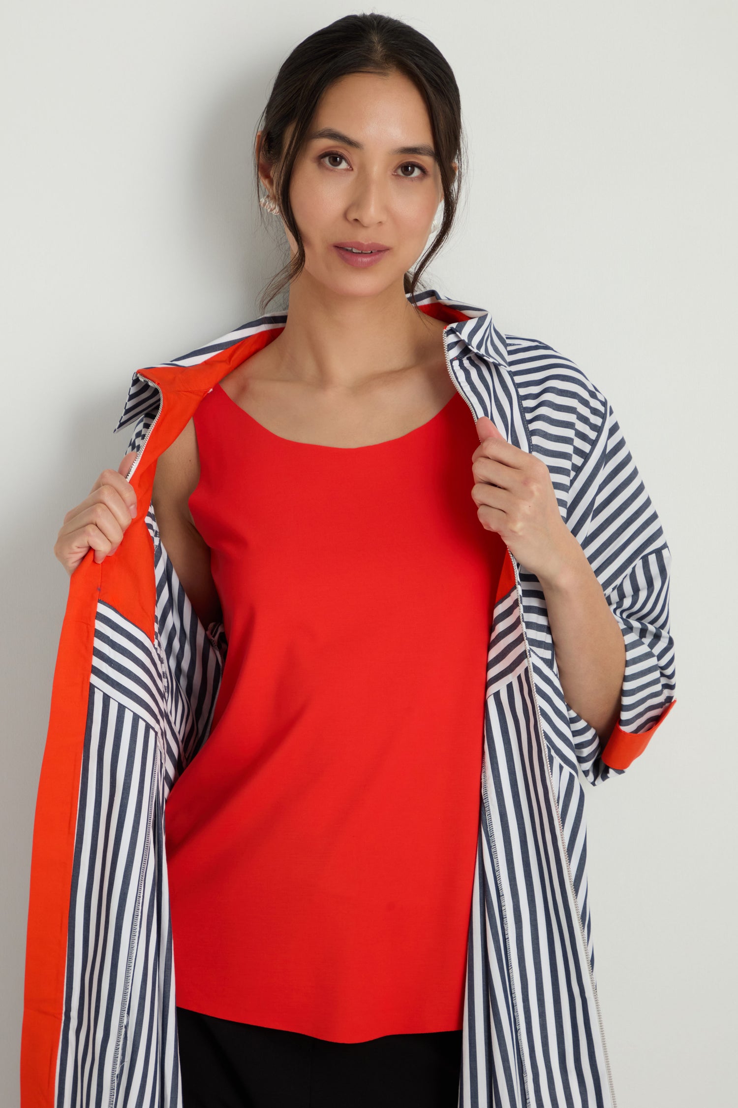 A woman stands against a light background wearing the Sleeveless Chilli Jersey Top and an open striped jacket with orange lining, looking at the camera.