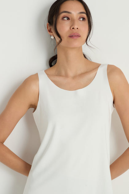 A woman with long dark hair pulled back is wearing the Sleeveless White Jersey Top, standing against a plain white background and looking slightly to the side.