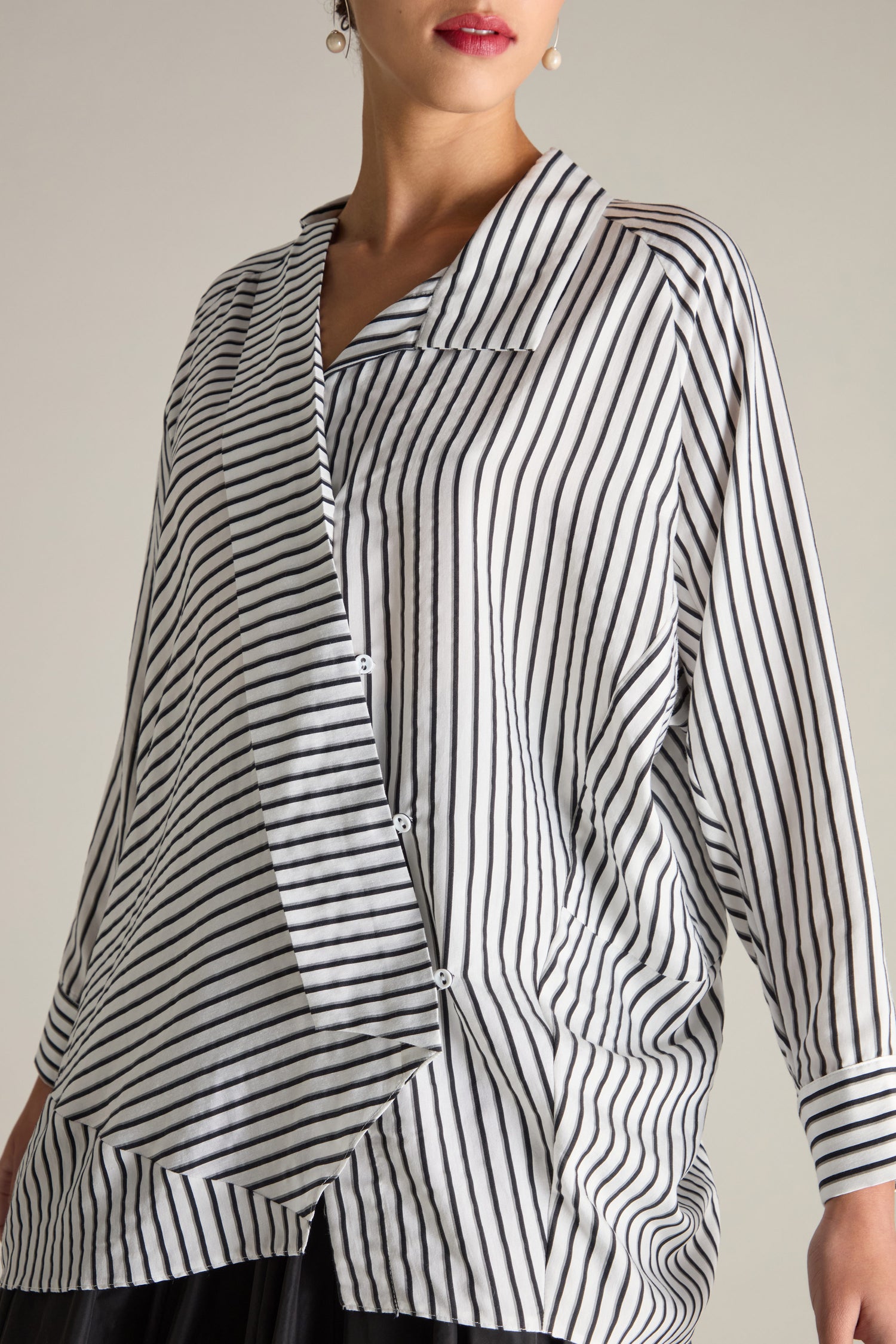 A person wearing the Stripe Asymmetric Shirt, a stylish contemporary button-up featuring black and grey stripes, an asymmetrical design, long sleeves, and a collared neckline.