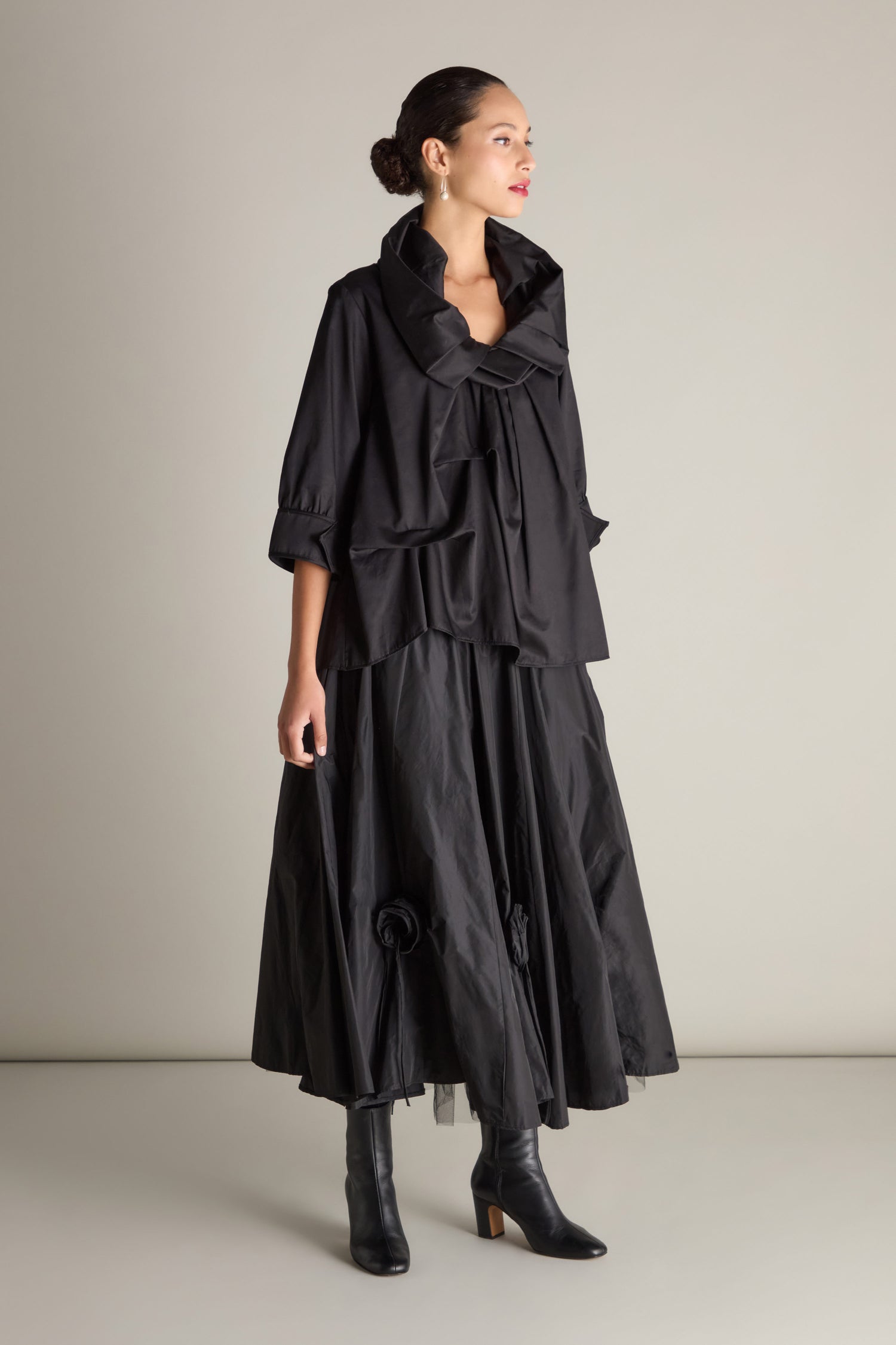 Person wearing a Frill Neck Easy Top with avant-garde tucking details, paired with black ankle boots and an ankle-length skirt against a plain backdrop.