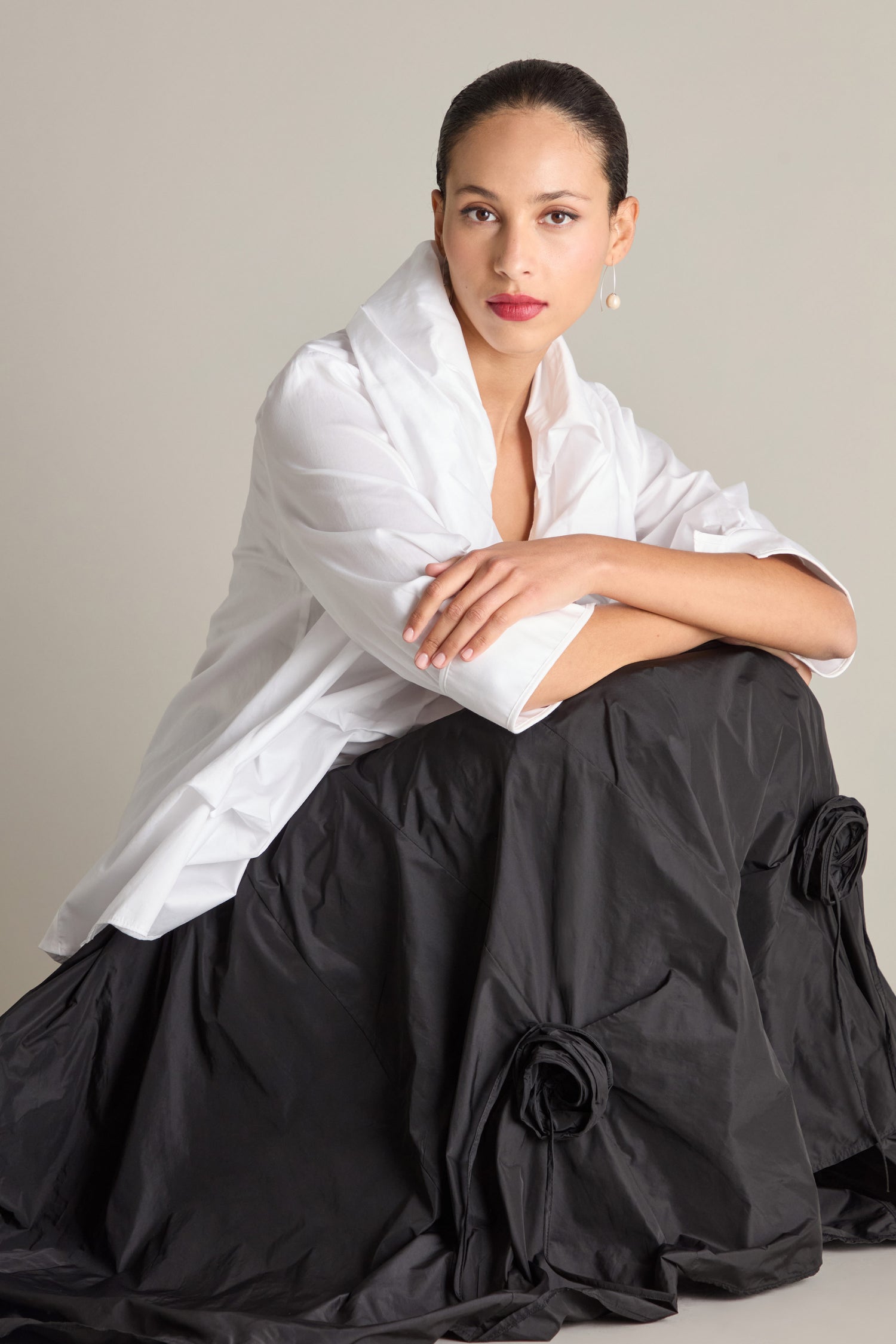 A person wearing the Frill Neck Easy Top and a black skirt with floral detailing sits with crossed arms on their knee, looking at the camera.