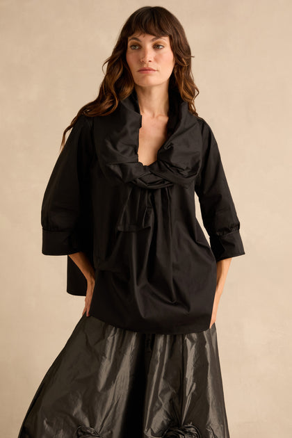A model wears the Black Frill Neck Easy Top, a black cotton top with three-quarter length sleeves, a relaxed silhouette, and a voluminous gathered cowl neckline.
