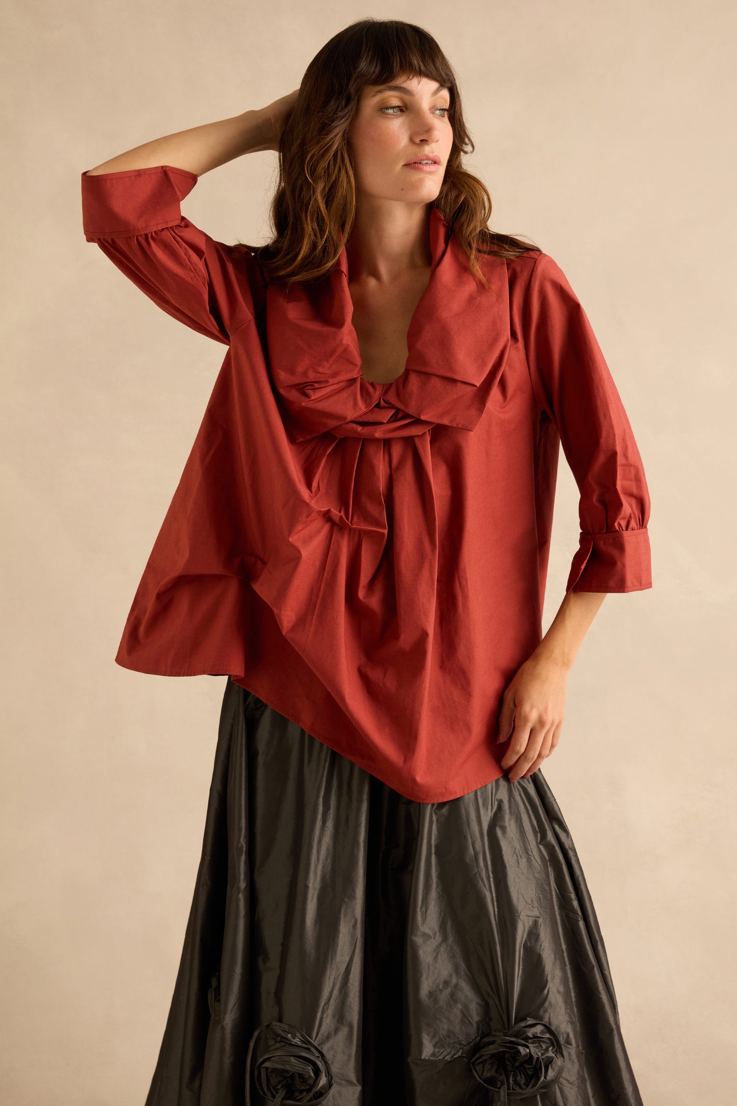 A woman wearing a Red Frill Neck Easy Top with a red cotton blouse featuring a wide, gathered frill collar and three-quarter sleeves, paired with a dark, textured midi skirt.