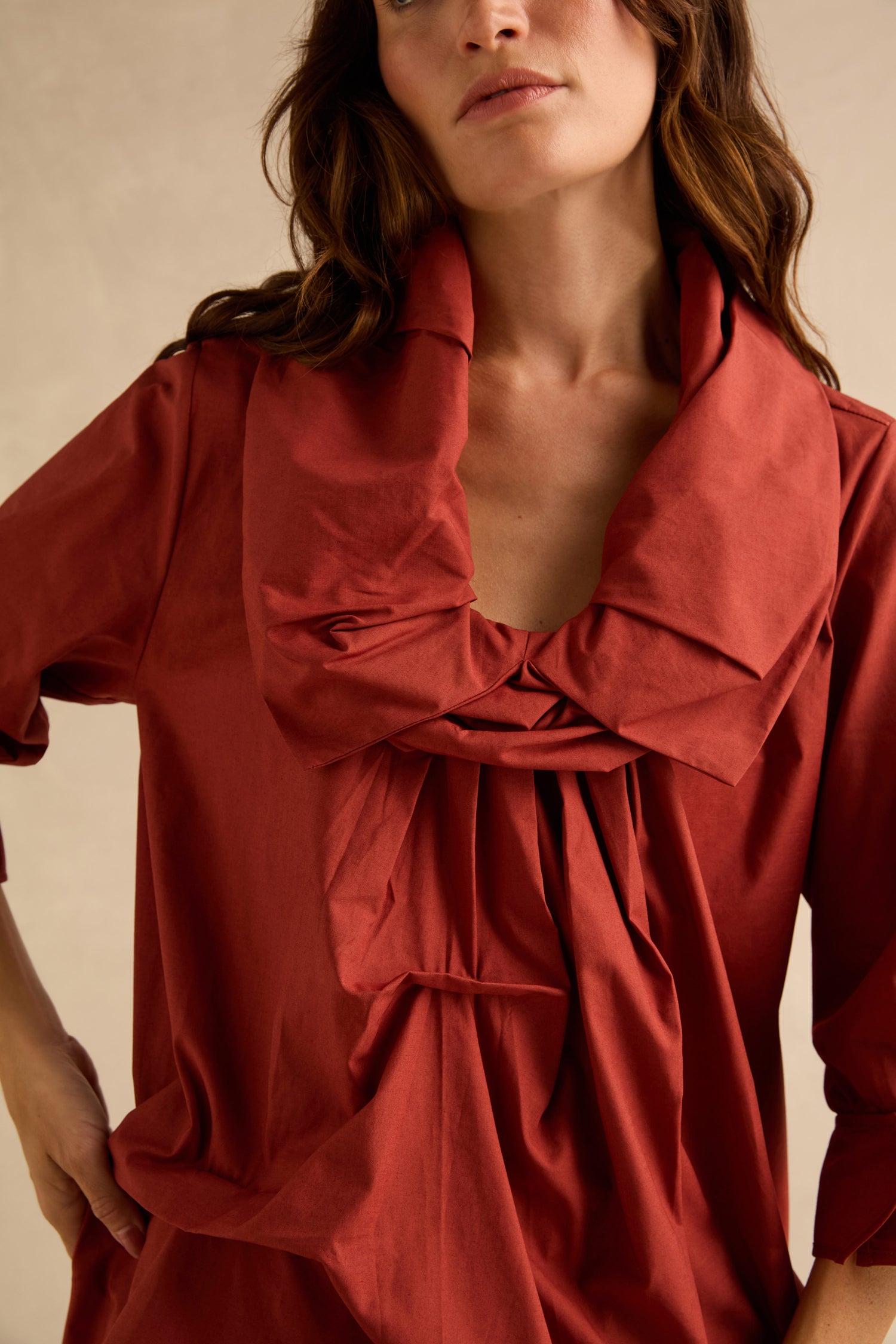 A person wears a rust-colored Red Frill Neck Easy Top featuring three-quarter sleeves, a large, pleated fold-over collar, and a gathered neckline.