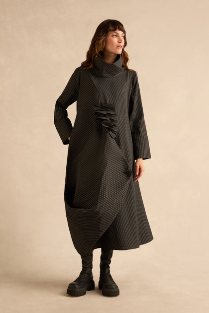 A woman wears a Pin Stripe Flower Detail Dress with a long-sleeved, pinstriped design, high collar, asymmetrical pleated bodice, bubble hem, and black platform boots.