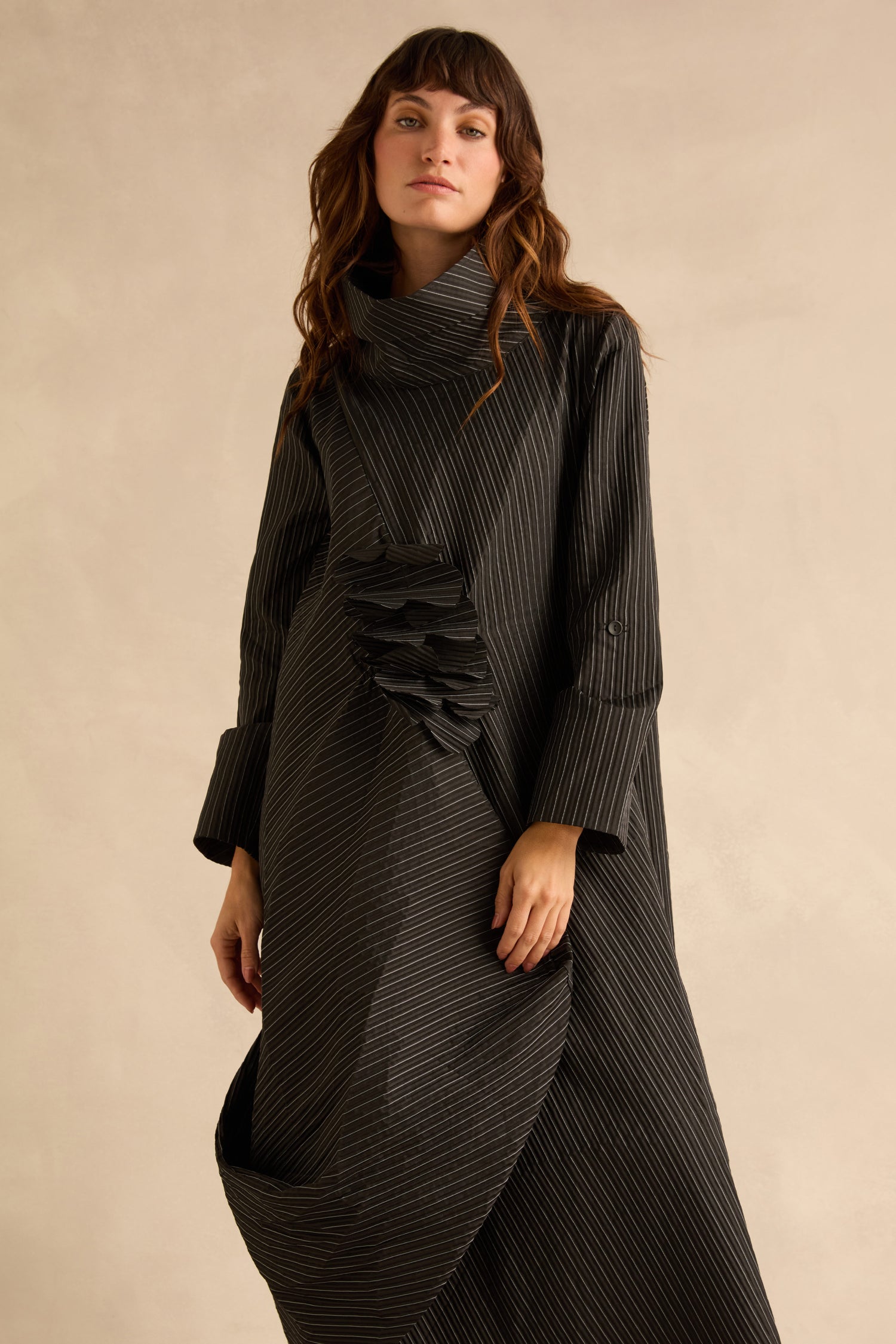A woman wears a Pin Stripe Flower Detail Dress, a long-sleeved, black pinstripe style featuring a high funnel neck and a gathered floral detail on the front.