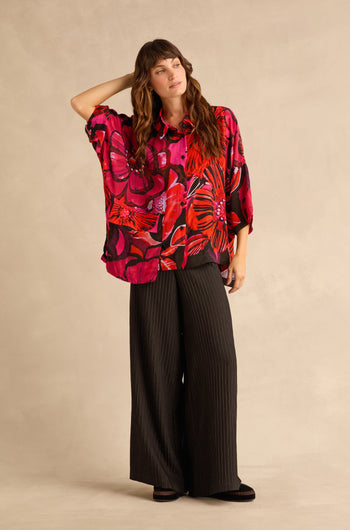 A person wears a vibrant red and black Pocket Floral shirt paired with wide-leg black pinstripe trousers.