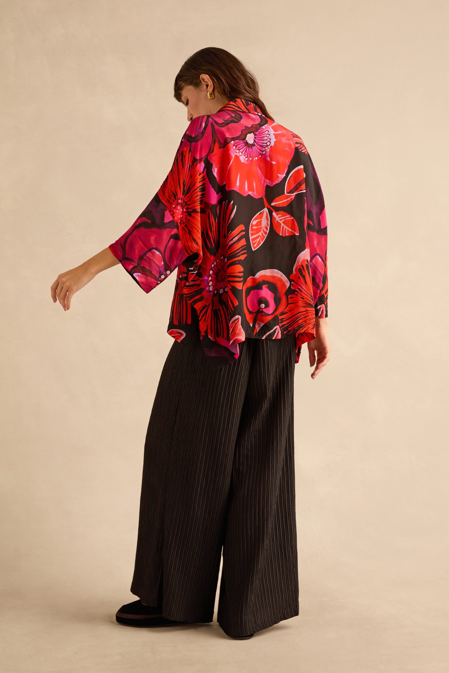 A person wearing a Pocket Floral Shirt in a vibrant red and black print paired with wide-leg black pleated trousers.