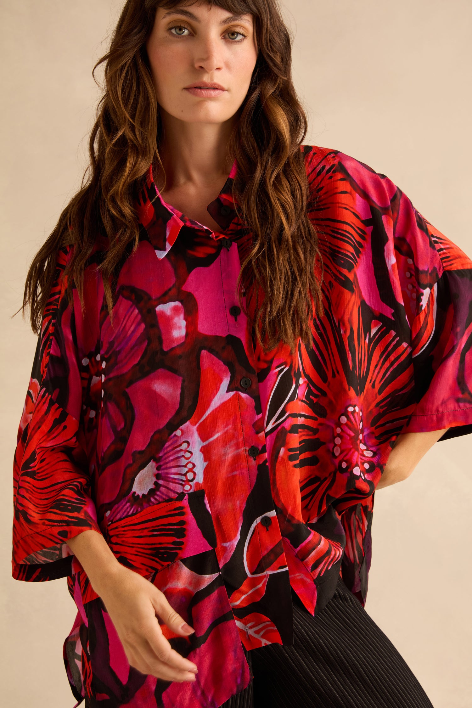 A person wearing an oversized viscose Pocket Floral Shirt featuring a vibrant red and pink floral pattern.
