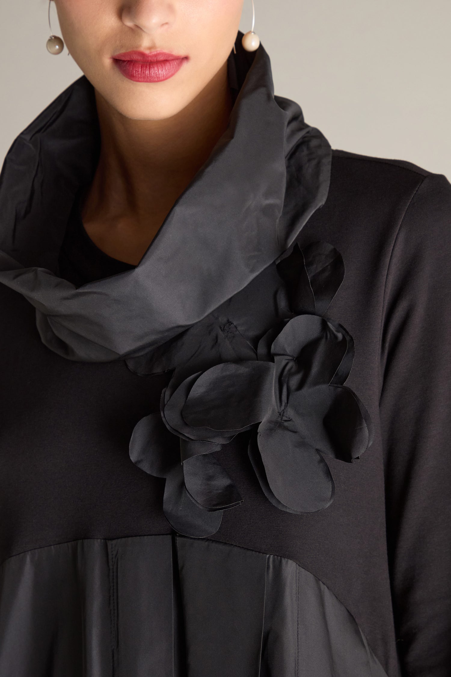 A person wearing the Jersey Taffeta Flower Dress in black, which features a high neck, side flower embellishments, and an empire waistline.