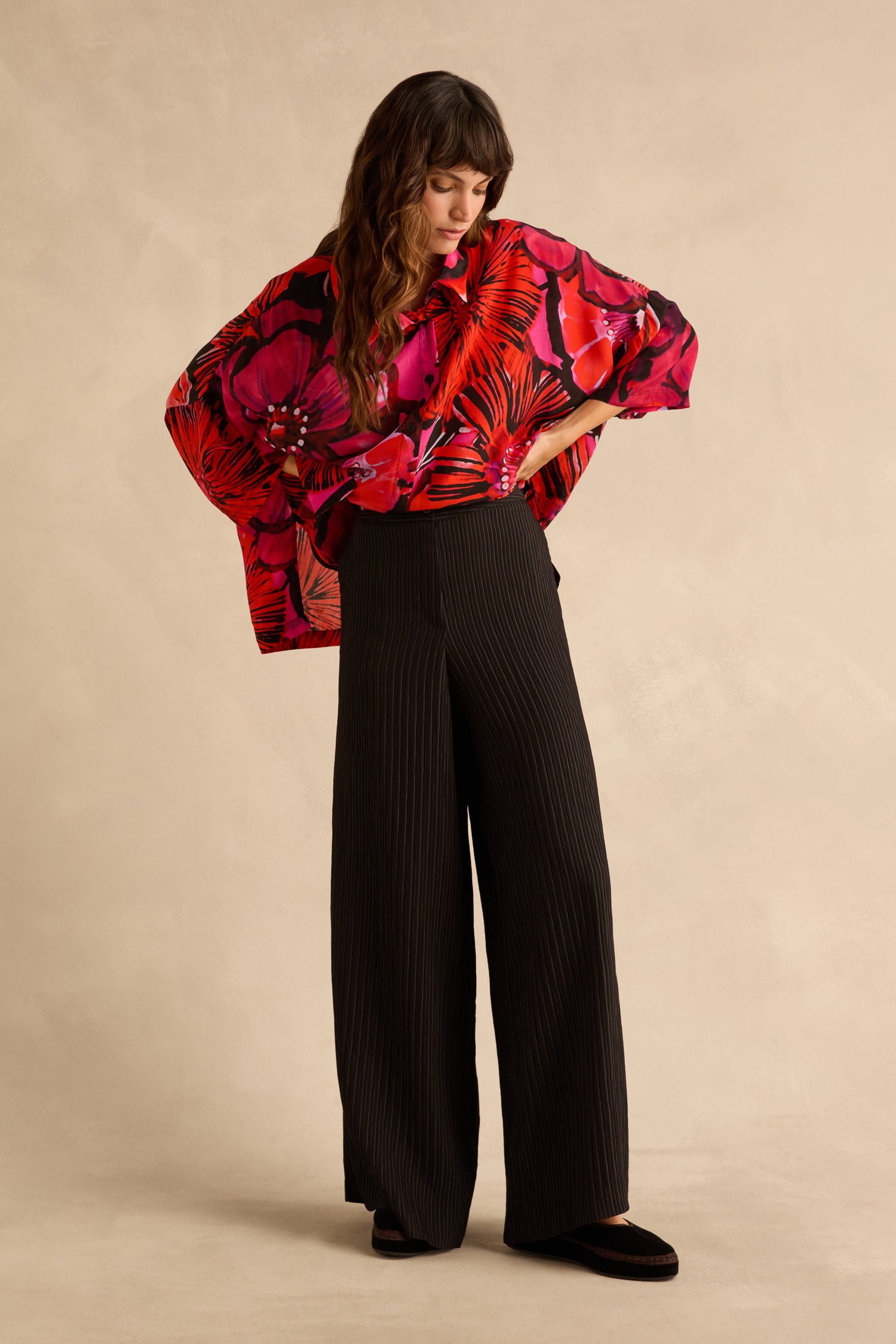 A person wearing a bright red and pink floral print blouse and black Pin Stripe Wide Leg Trousers.