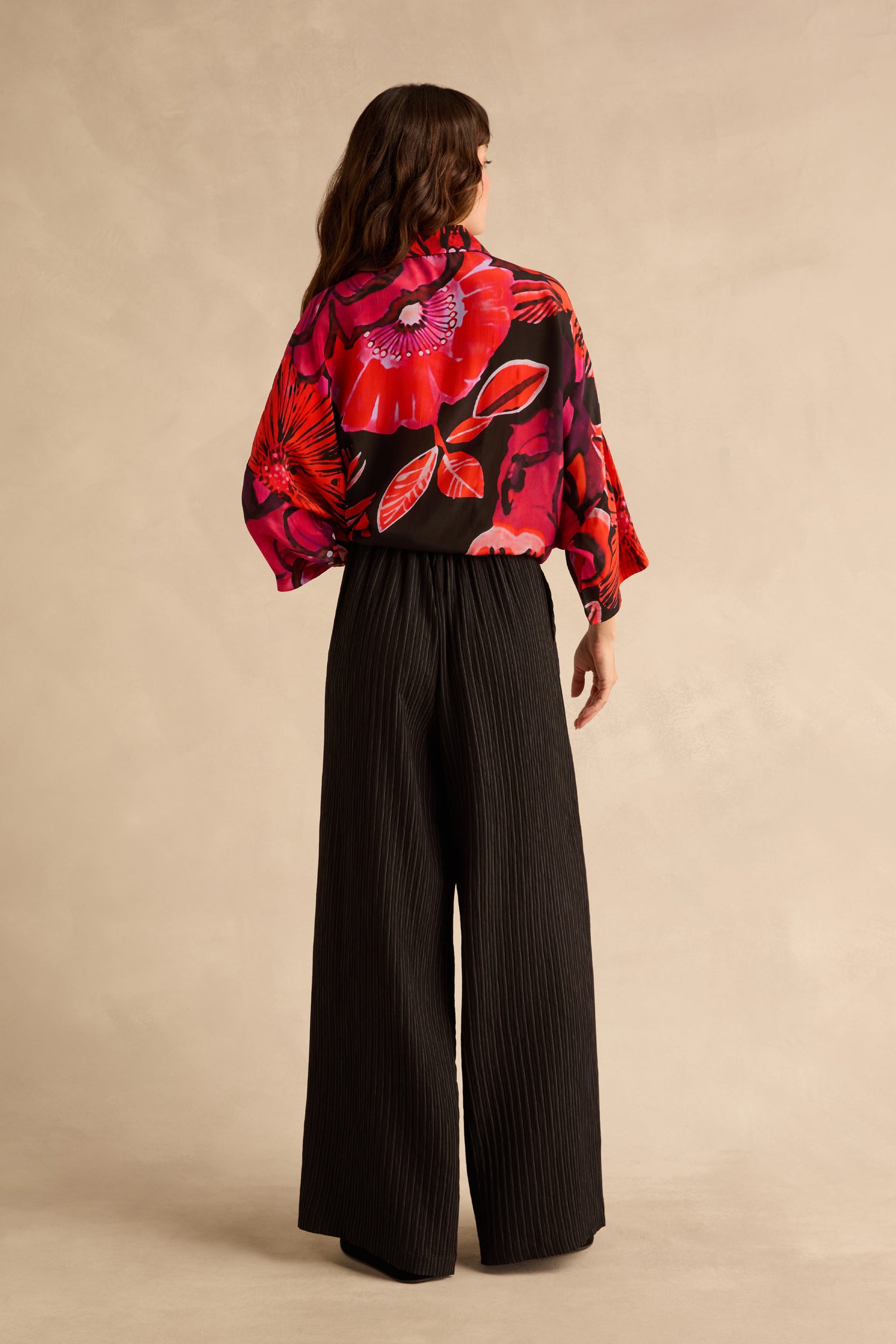 A person seen from behind, wearing a black top with a red and pink floral pattern and black Pin Stripe Wide Leg Trousers.