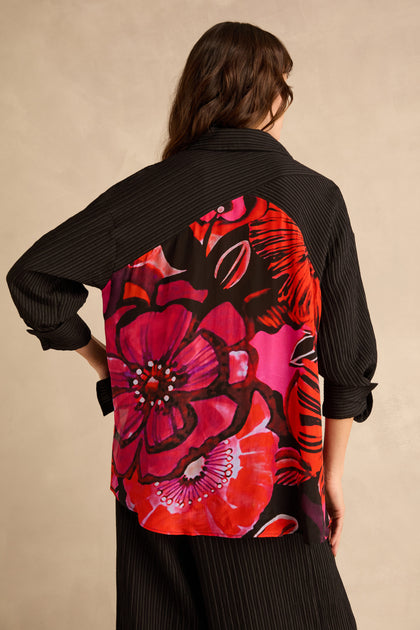 Back view of a person wearing a black Flora Pin Stripe Shirt, a relaxed fit button-down with a large, vibrant red and pink floral print panel on the back.