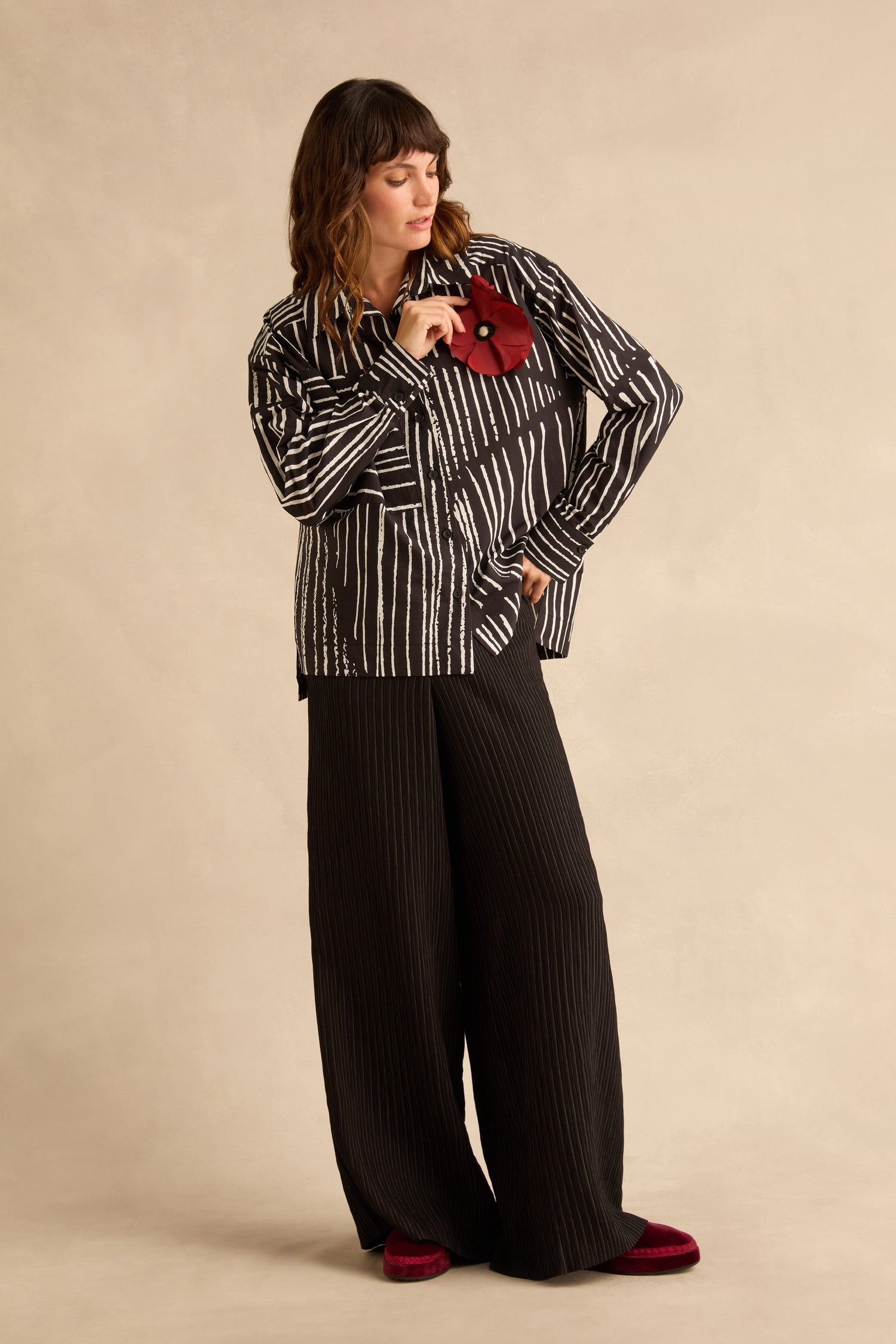 A person wearing a Linear Shirt With Flower Pin in a black-and-white linear print with black wide-leg trousers.
