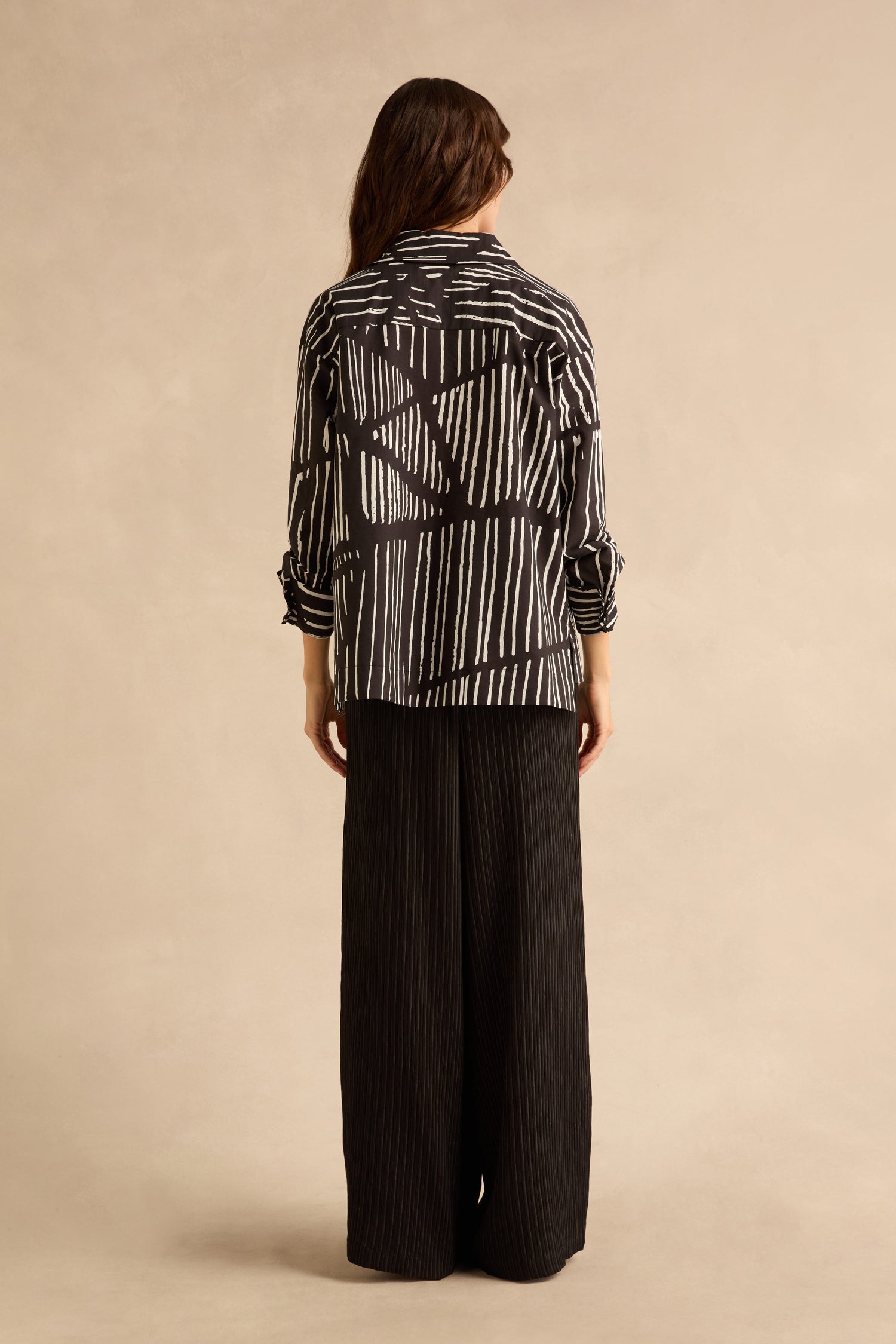 Viewed from behind, a person wears a black and white Linear Shirt With Flower Pin paired with wide-leg black trousers.