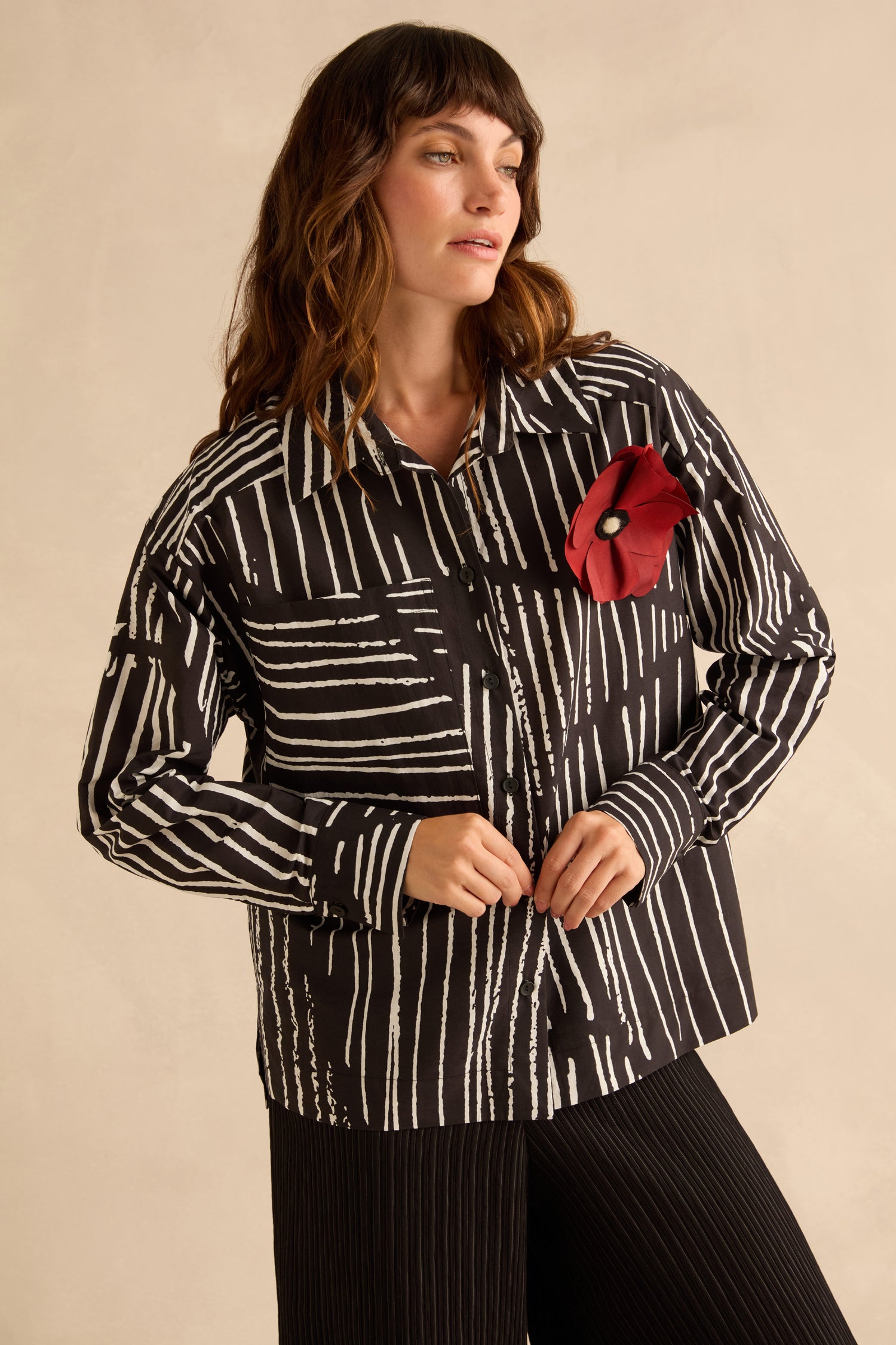 A person wearing a Linear Shirt With Flower Pin, featuring a black and white linear print and a large red flower pin on the chest.