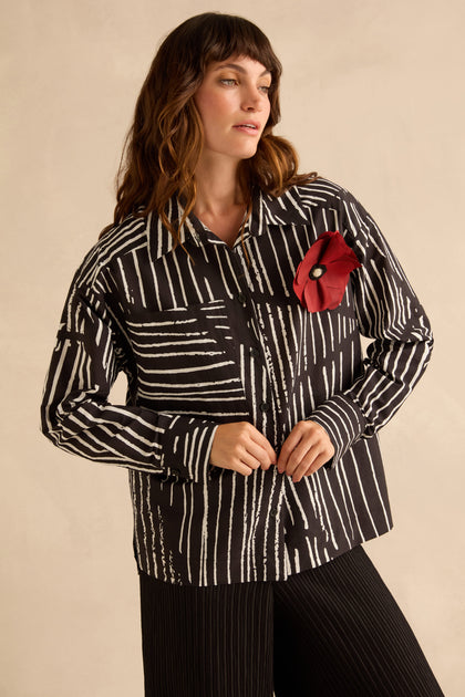 A person wearing a Linear Shirt With Flower Pin, featuring a black and white linear print and a large red flower pin on the chest.