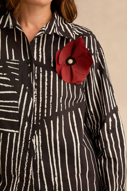Linear Shirt With Flower Pin in black and white linear print with vertical stripes and a large red flower pin on the chest.