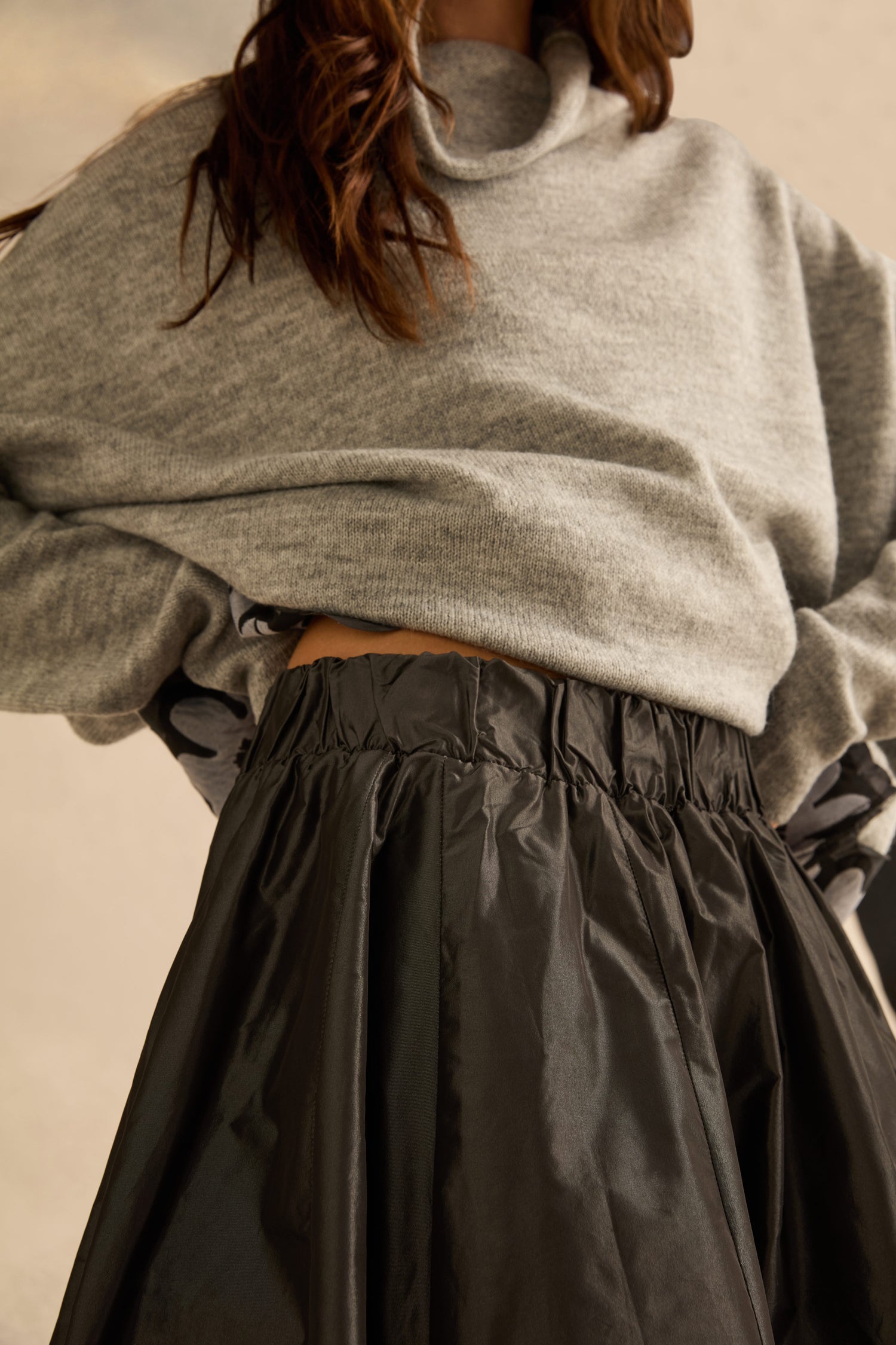 A person wearing a metallic grey sweater tucked into a black Flower Detail Taffeta Skirt with a gathered elastic waistband.