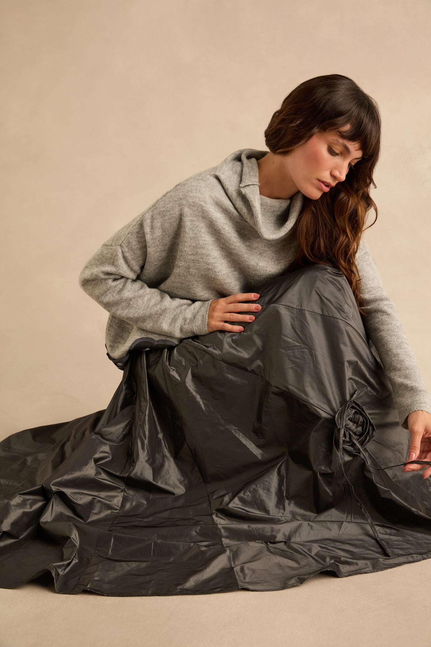 A person wearing a grey cowl-neck sweater and a metallic grey Flower Detail Taffeta Skirt with a drawstring flower detail.