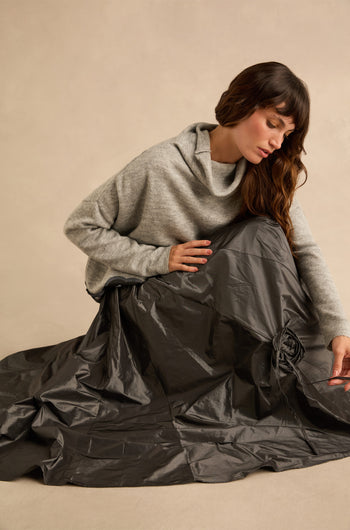 A person wearing a grey cowl-neck sweater and a metallic grey Flower Detail Taffeta Skirt with a drawstring flower detail.