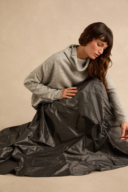 A person wearing a grey cowl-neck sweater and a metallic grey Flower Detail Taffeta Skirt with a drawstring flower detail.