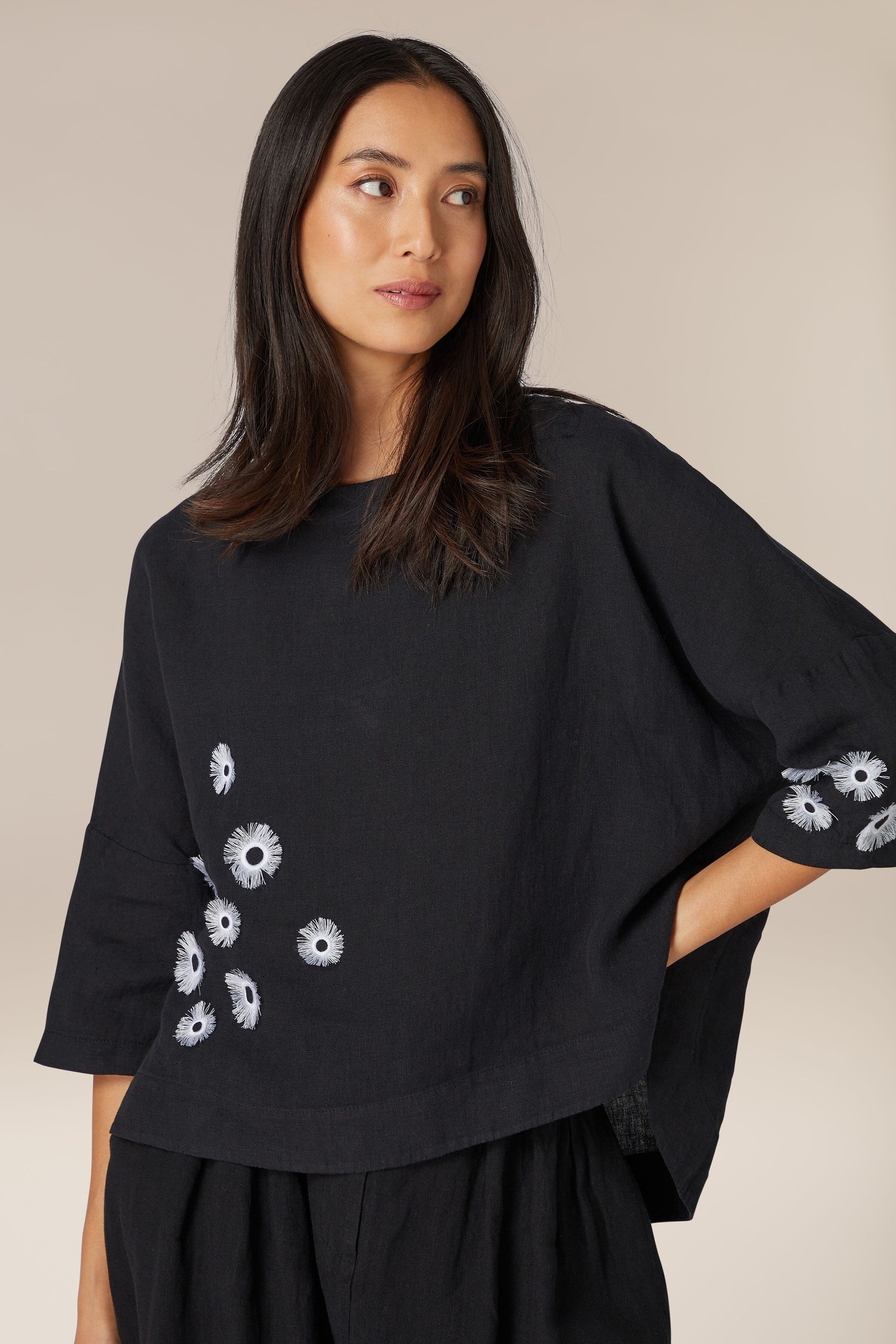 Woman in a Daisy Linen Top with high boat neck and floral embroidery, looking to the side.