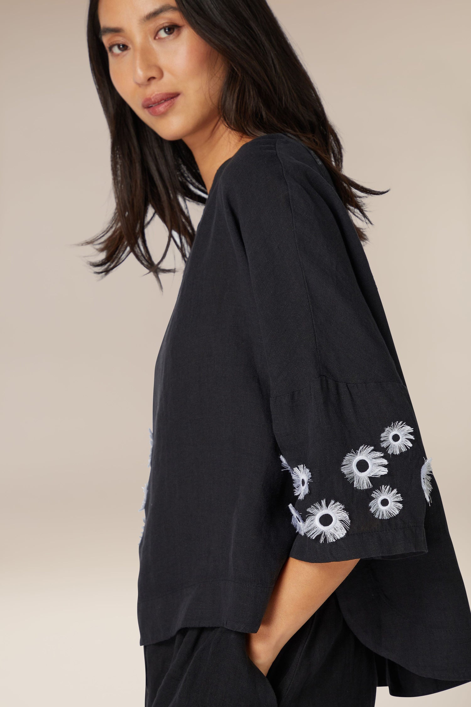 Woman showcasing a Grace Linen Top with avant-garde design, featuring high boat neck and floral embroidery on the sleeve.