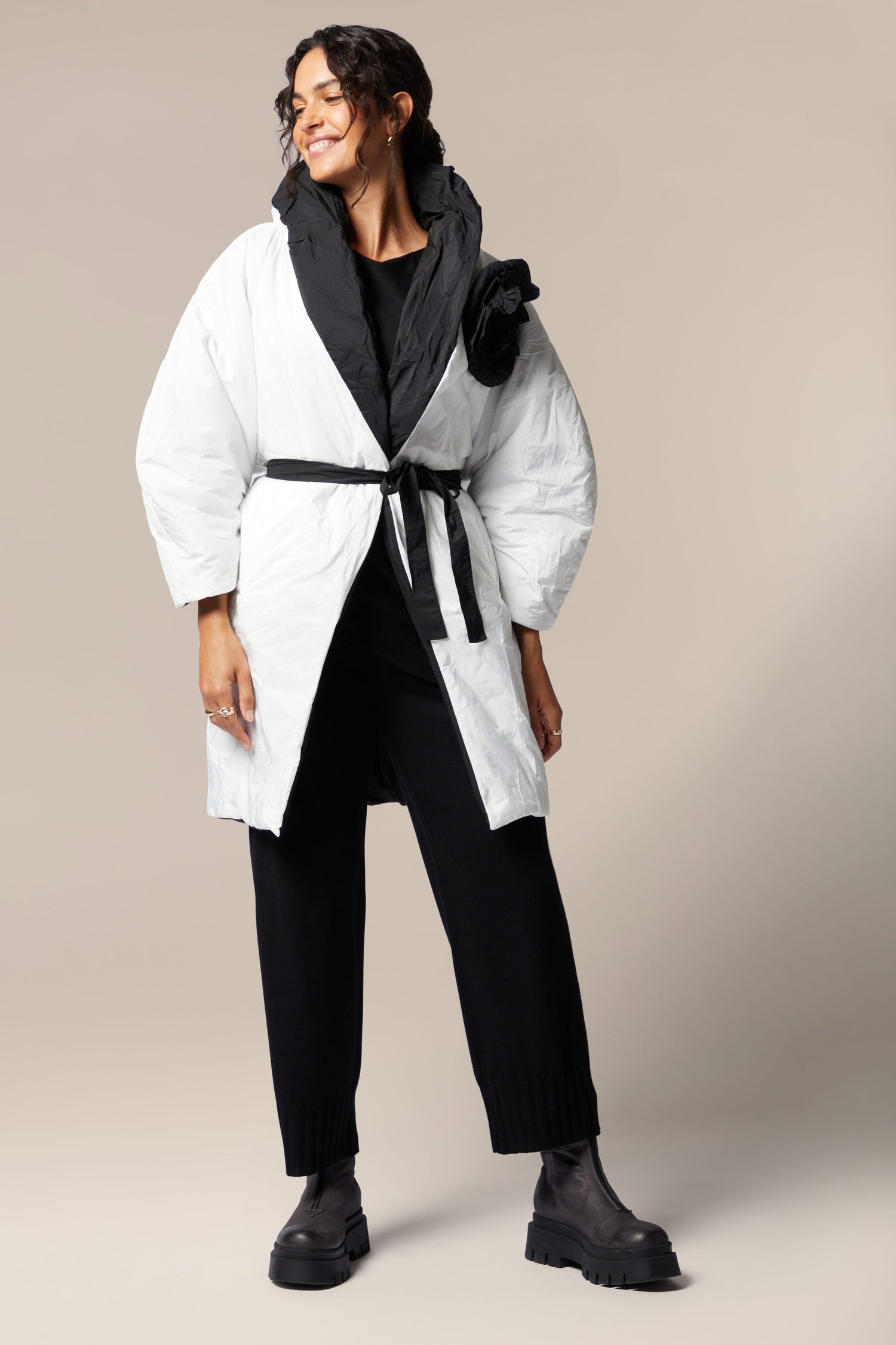 A woman wearing a white Reversible Puffa decorated with flower applique, paired with black pants.