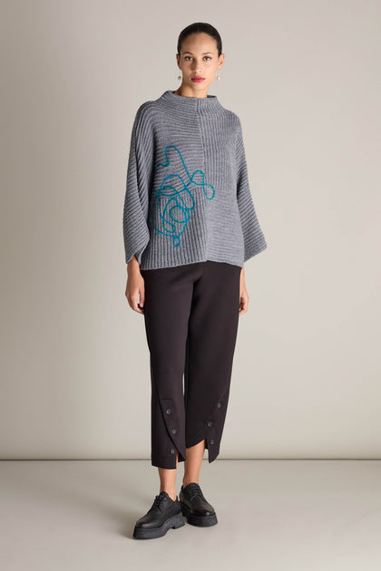 A person wearing a gray Topstitch Detail Rib Knit sweater with a blue pattern, black cropped pants, and black shoes stands against a neutral background.