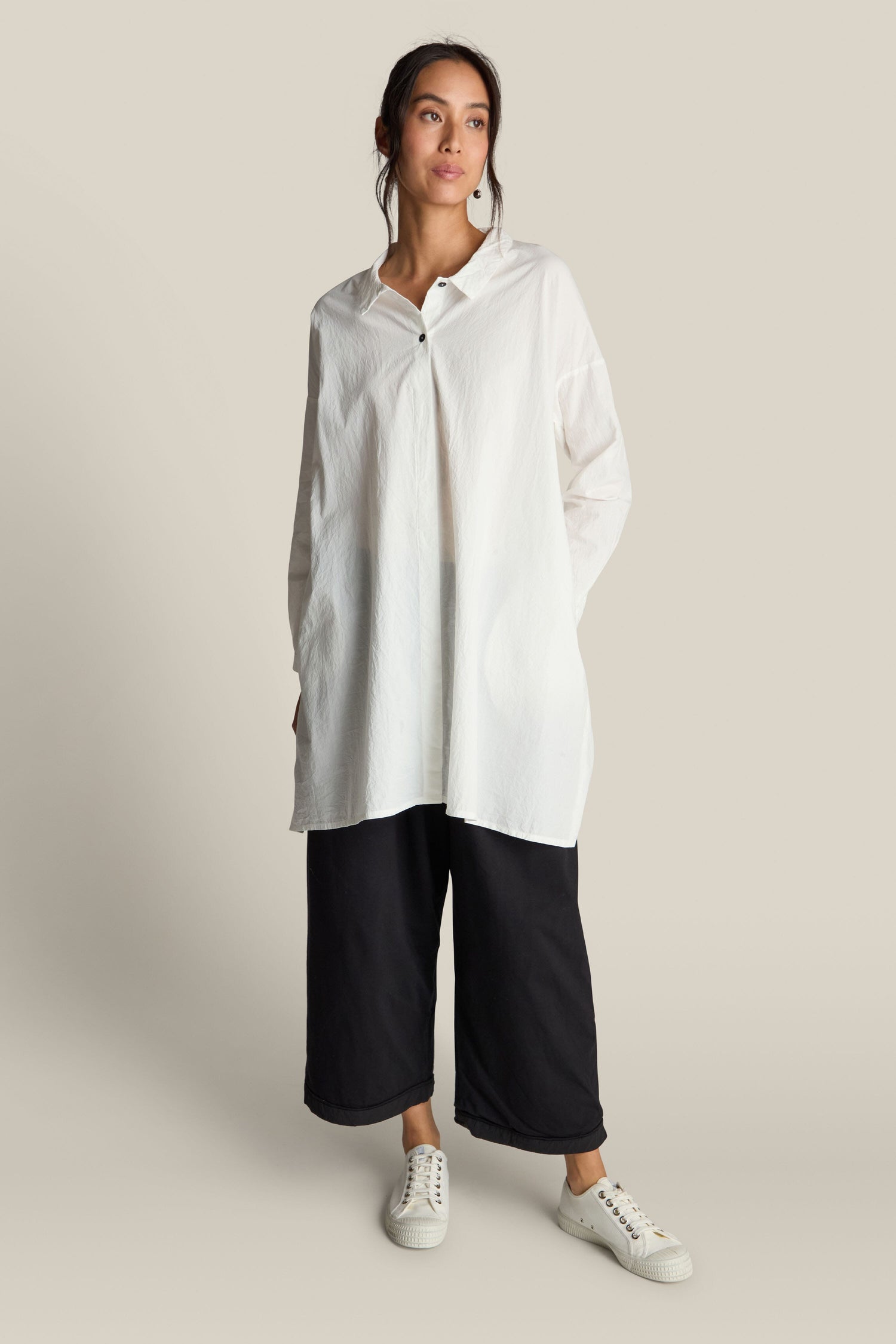 A person is wearing an **Oversize Shirt** made from premium white cotton, paired with black wide-legged pants and white sneakers, posing against a plain background.