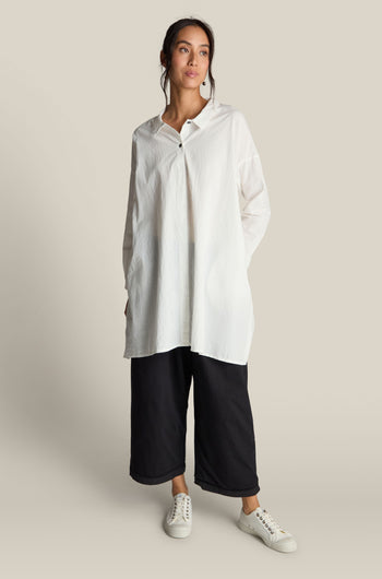 A person is wearing an **Oversize Shirt** made from premium white cotton, paired with black wide-legged pants and white sneakers, posing against a plain background.