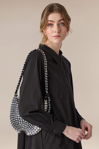 A woman wearing a black shirt and carrying a black and white woven Bellani Small Bottletop Handbag, handcrafted in Brazil.