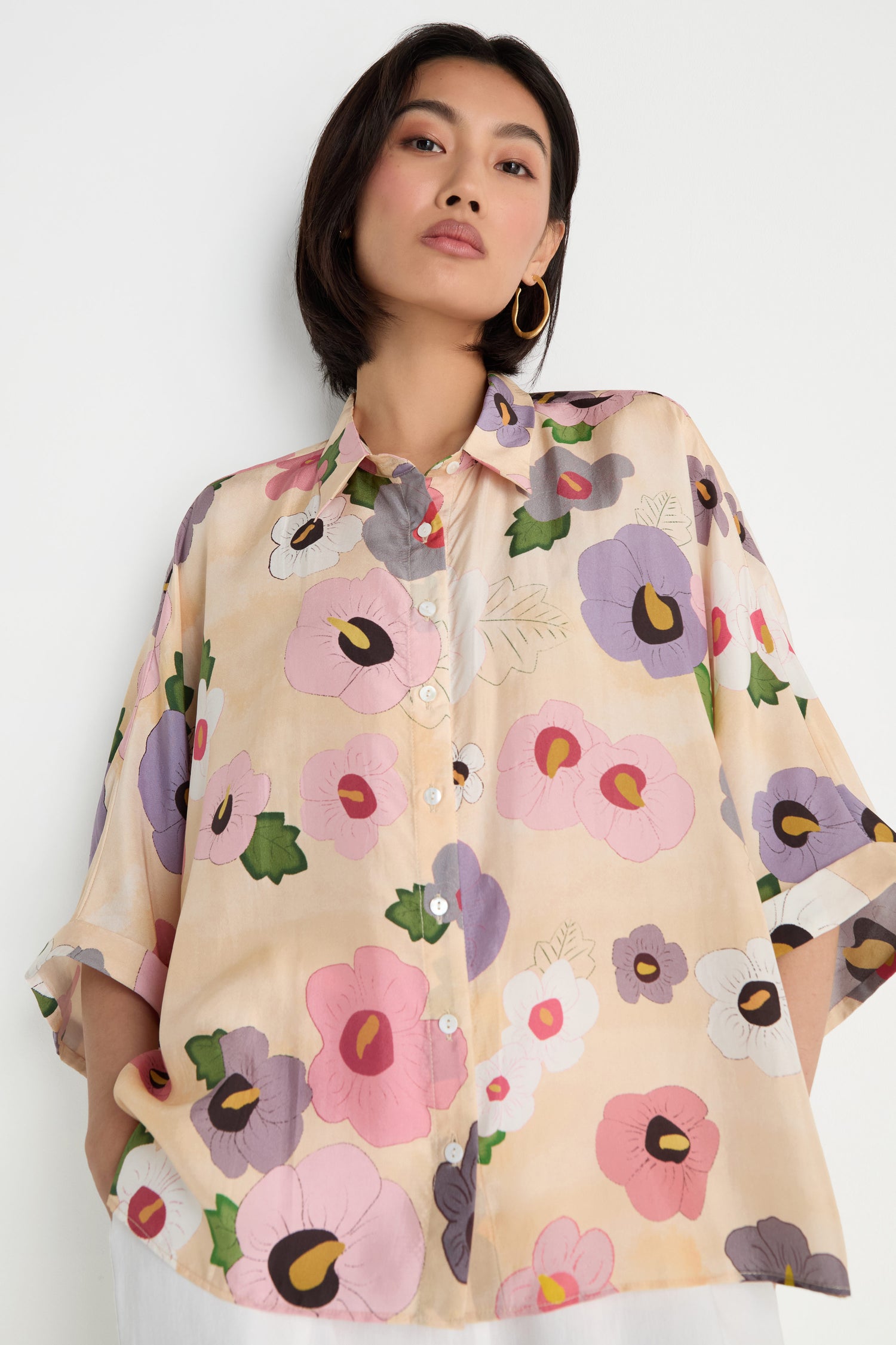 A woman wears the Rose Eclipse Silk Boxy Shirt with a modern graphic floral print, standing against a plain white background.