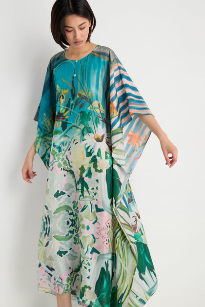 A person wears the Fern Silk Kaftan, featuring a loose, flowing fit and a colorful abstract botanical print, standing against a plain white background.