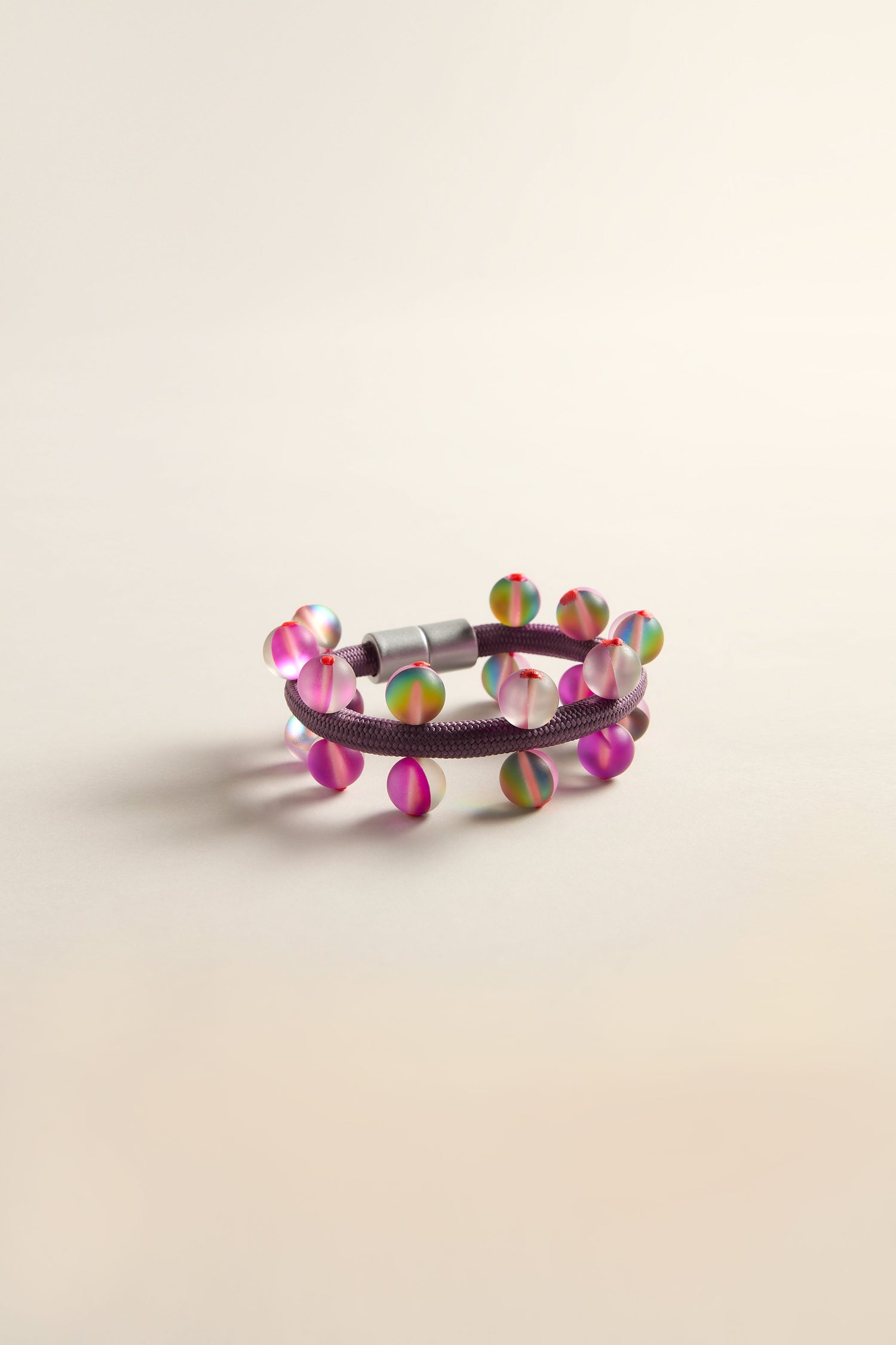 The Atmosphere Bracelet by Christina Brampti is a modern jewelry piece with multicolored round beads on a vibrant purple band, elegantly displayed against a light background.