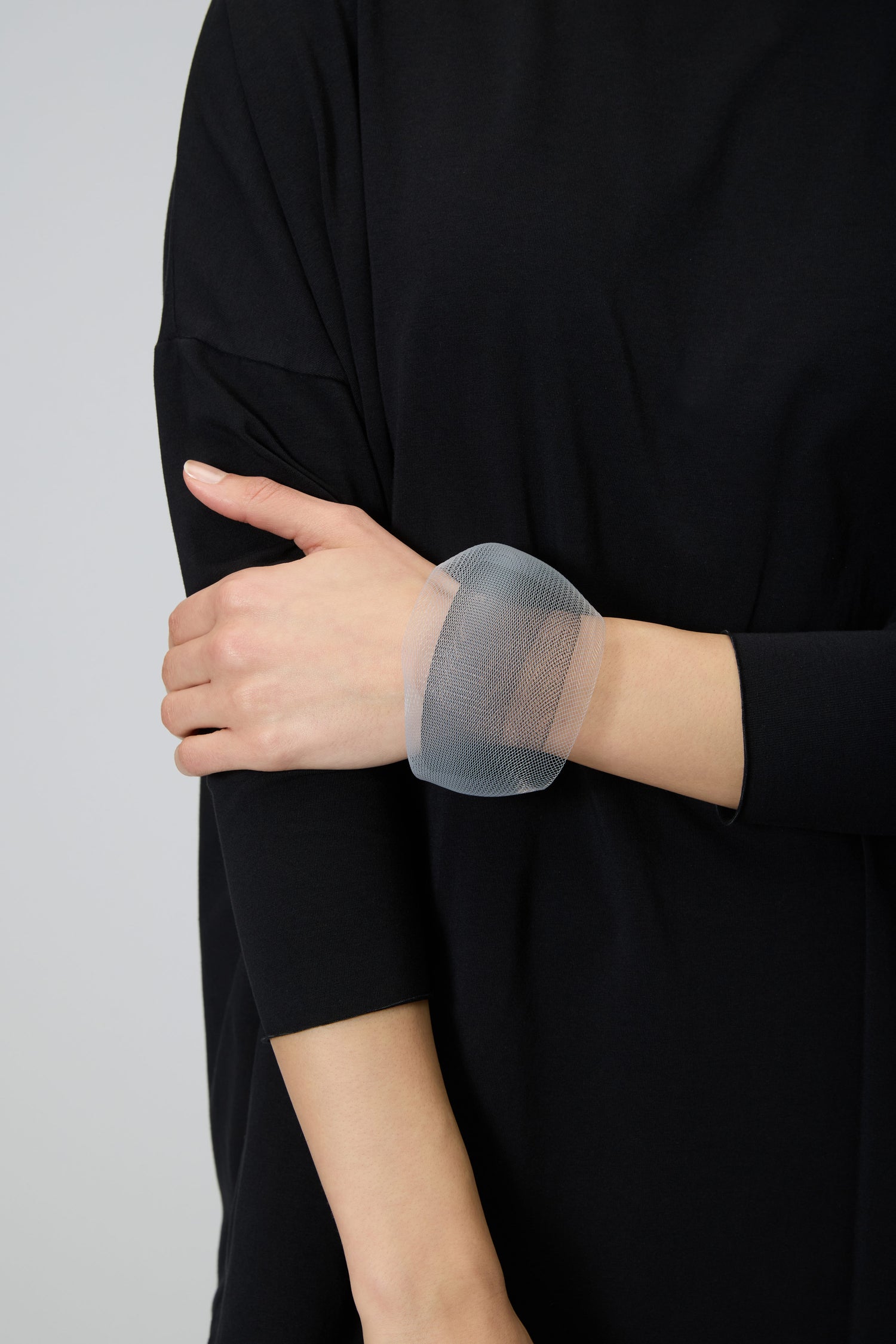 Wearing a loose-fitting black top, the person accents their look with the Silver Statement Mesh Bracelet, a bold piece of modern jewellery featuring sculptural silver mesh on their wrist.