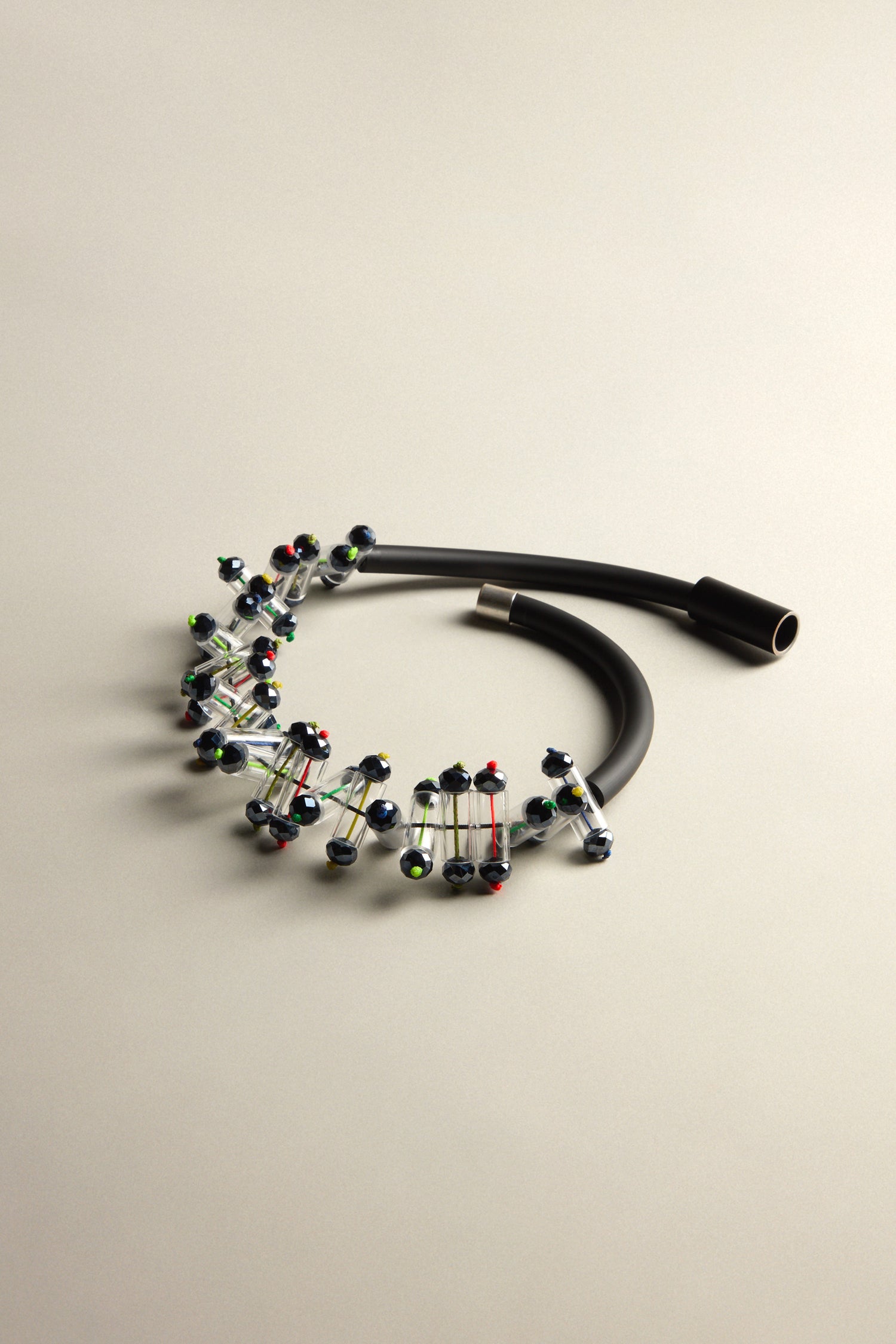 The Matrix Necklace features a black cable with decorative metal wire resembling a DNA strand and colorful beads, creating a futuristic piece against a neutral background.