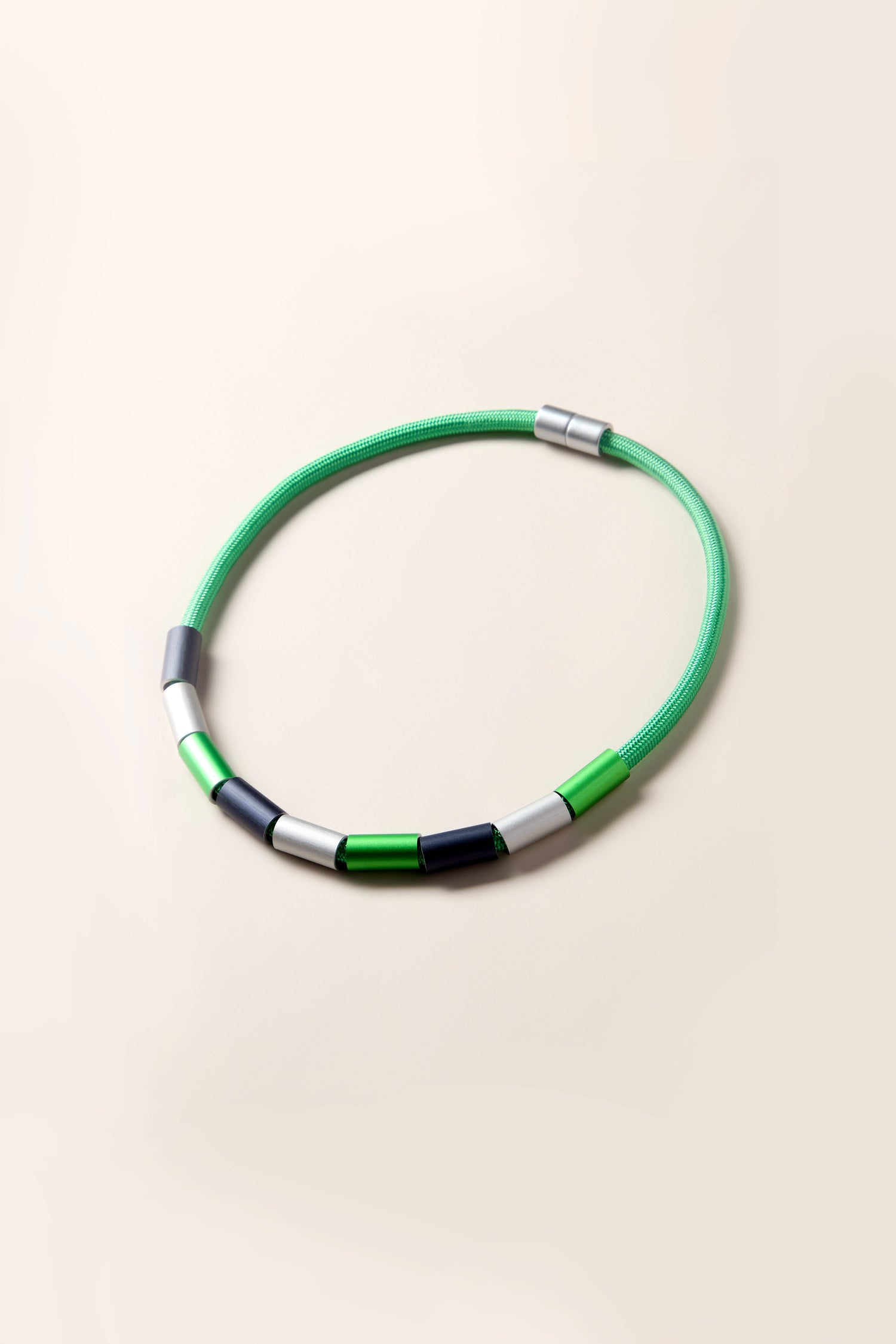 An Aluminium Cylinders Necklace featuring a flexible design with alternating sections of green, white, black, and metallic grey, reminiscent of a contemporary Christina Brampti creation.