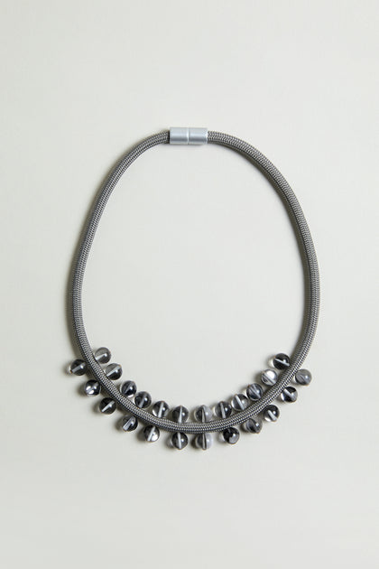 The Smoke Atmosphere Necklace features a metallic textured chain with shiny oval metal beads along the lower half. Lightweight and modern, it's ideal for everyday wear. Shown on a plain light background.