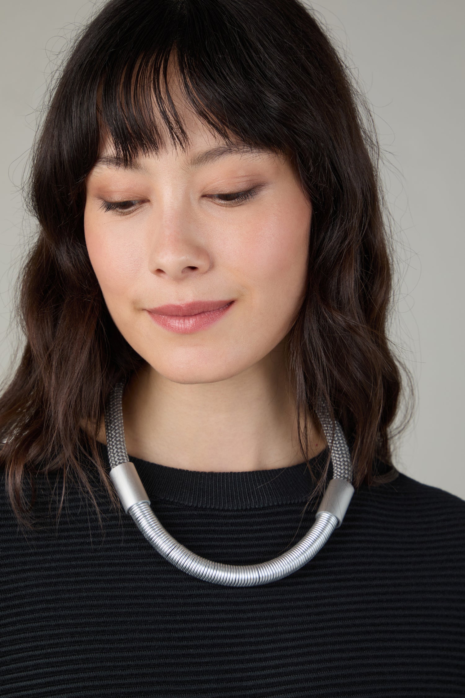 A woman with shoulder-length dark hair and bangs wears a black striped top and the Flow Cord Necklace, embodying contemporary style as she looks down with a neutral expression.