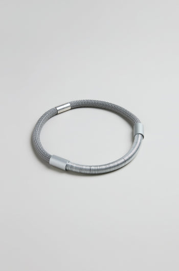 The Flow Cord Necklace features a textured mesh cord with smooth metal accents, embodying sleek contemporary style. Shown against a plain light gray background.