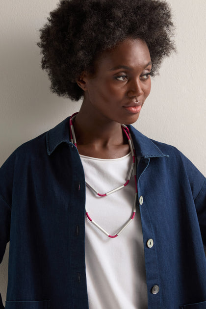 Person wearing a blue jacket over a white shirt, accessorized with the Long Cylinders Necklace that showcases contemporary design, standing against a white background.