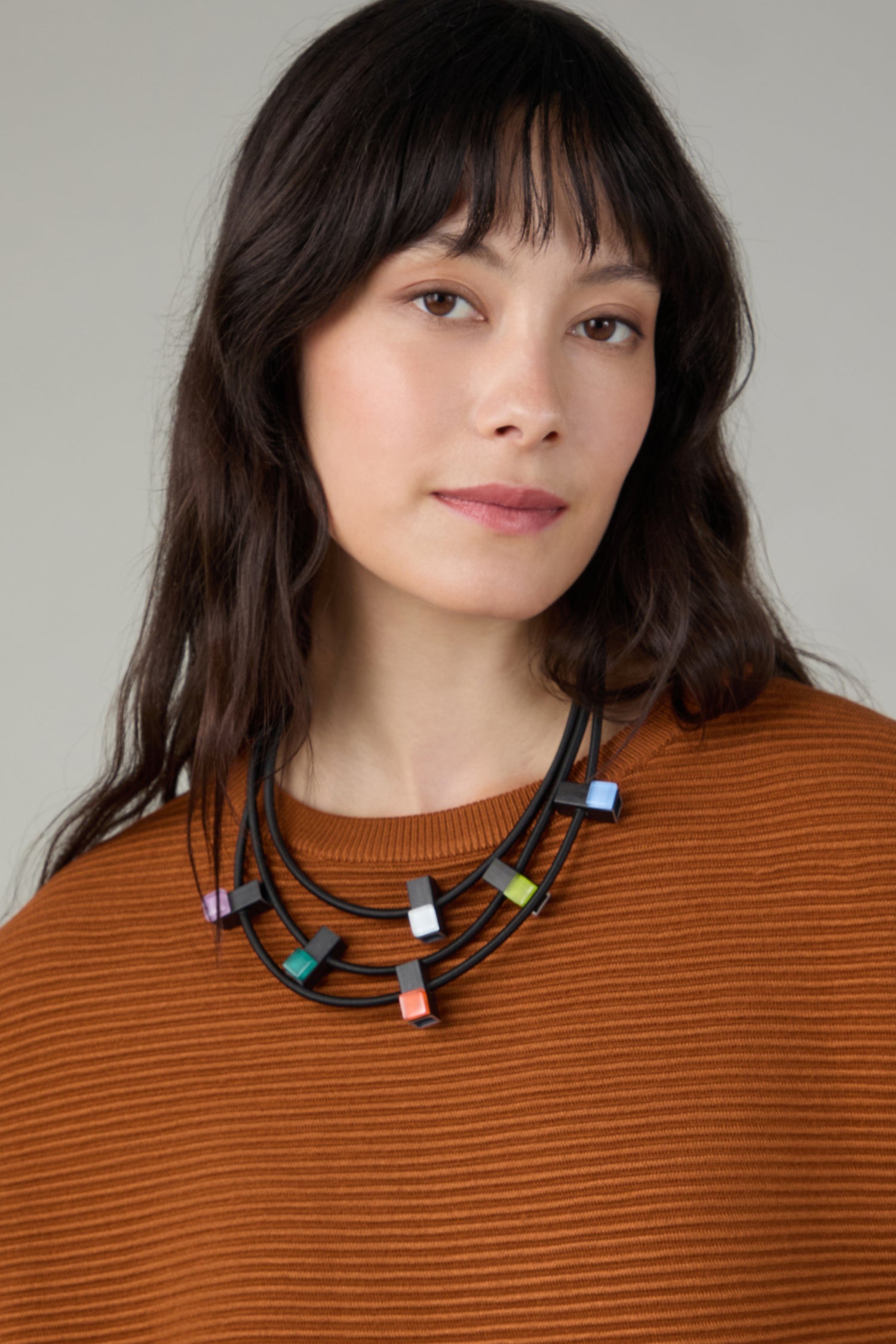 A woman with long dark hair wears a rust-colored ribbed top and the Colour Pop Glass Beads Necklace, looking at the camera with a neutral expression.