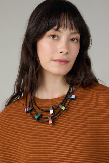 A woman with long dark hair wears a rust-colored ribbed top and the Colour Pop Glass Beads Necklace, looking at the camera with a neutral expression.
