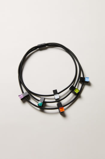 Three Colour Pop Glass Beads Necklaces by Christina Brampti, each with a black cord and a single vibrant square bead in purple, green, orange, blue, or white. Modern statement jewellery perfect for any occasion.
