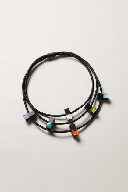 Three Colour Pop Glass Beads Necklaces by Christina Brampti, each with a black cord and a single vibrant square bead in purple, green, orange, blue, or white. Modern statement jewellery perfect for any occasion.