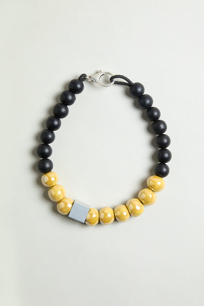 The Elements Necklace is a bold contemporary piece with black beads on one side, yellow marbled beads on the other, a rectangular silver accent, and a silver clasp—ideal for lovers of sculptural ceramic-inspired jewelry.
